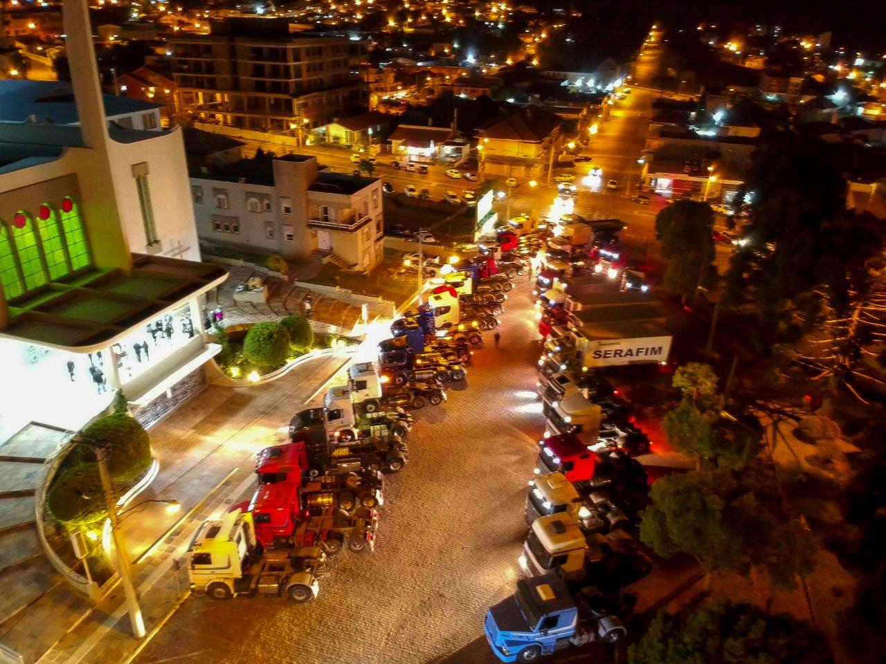 Vista aérea noturna da Igreja Matriz de São Marcos iluminada, com bolsas de caminhões enfileirados em frente ao templo para a vitória tradicional dos motoristas durante o lançamento do cartaz da Festa de Nossa Senhora Aparecida e dos Motoristas. Foto: divulgação da Festa