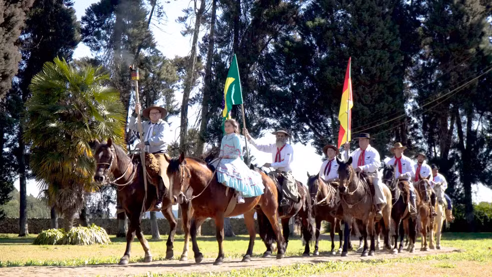 Imagem mostra momento da gravação do clipe oficial da Chama Crioula 2025, com cavaleiros conduzindo o fogo simbólico e artistas tradicionais gaúchos reunidos em ambiente rural, em Vacaria (RS), para homenagear a geração e acendimento da chama dos Festejos Farroupilhas.| Foto: Divulgação/ Guaiaca Record's